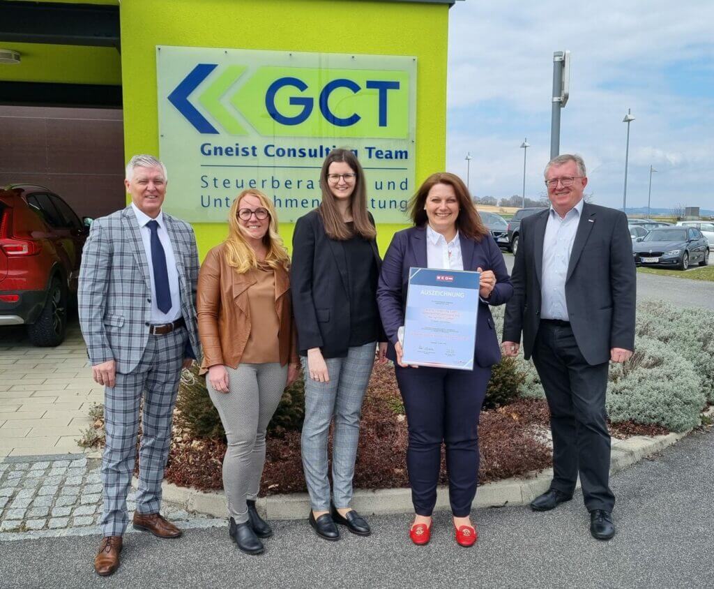Gruppe von fünf Geschäftspersonen vor dem GCT-Gebäude, freudig eine Auszeichnung präsentierend, symbolisiert Erfolg in der Steuerberatung und Gewinn "Familienfreundlichstes Unternehmen Burgenland"