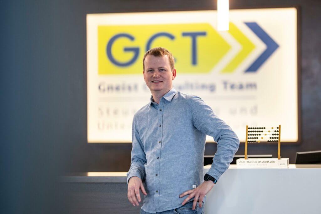 BMD Consultant Franz Gruber steht mit Hand in der Hüfte vor dem GCT Logo – professionell und präsent