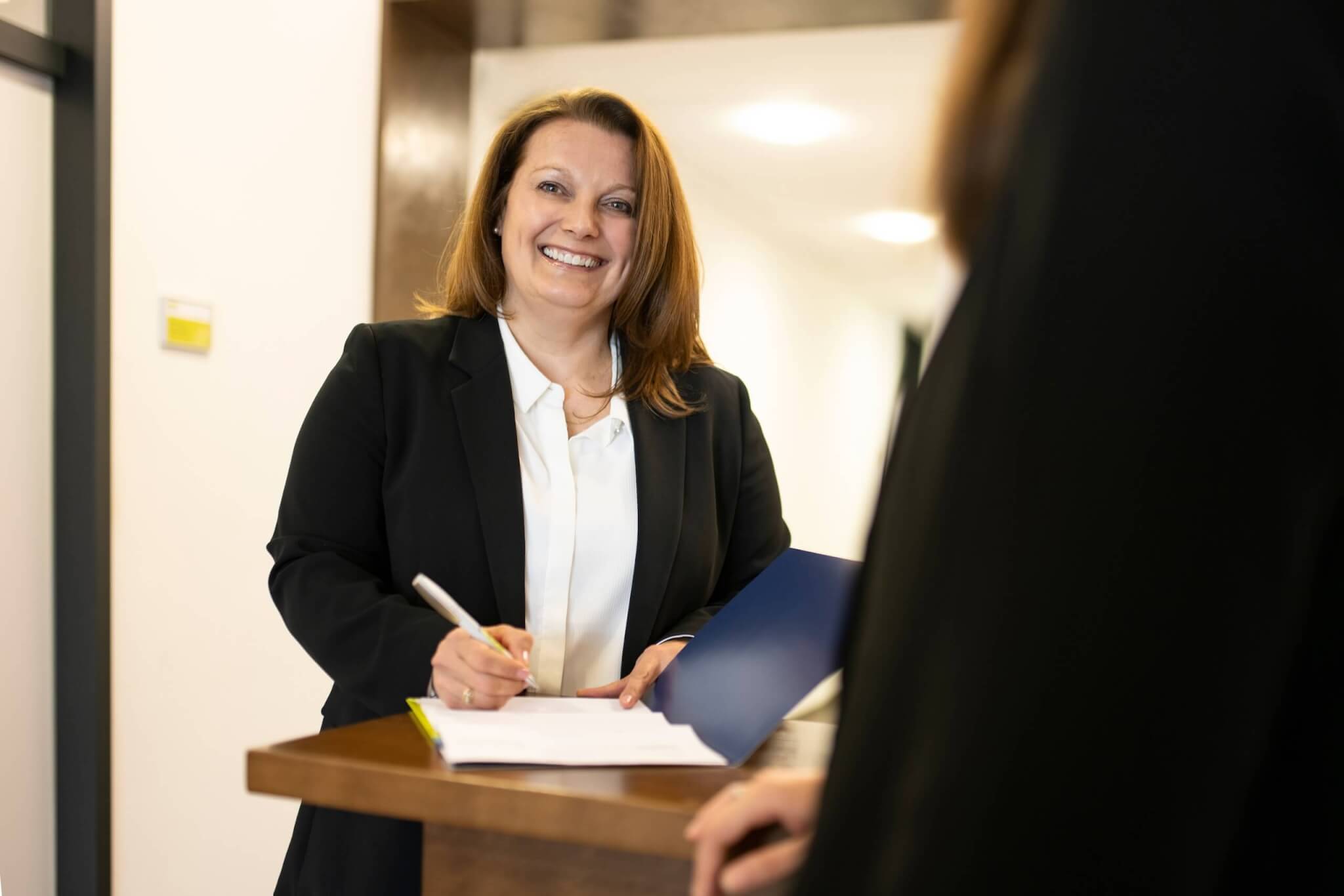 Personalverrechnerin steht hinter einem Pult und unterzeichnet einen Vertrag.