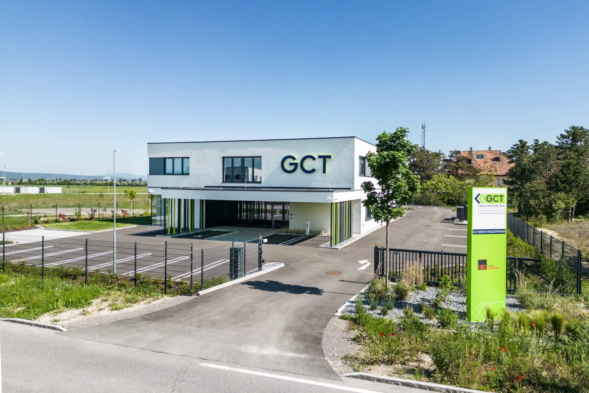Steuerberatung Wiener Neustadt: Modernes GCT Steuerberatungsgebäude mit Parkplatz und grüner Umgebung unter blauem Himmel. Effizienter Unternehmensservice.