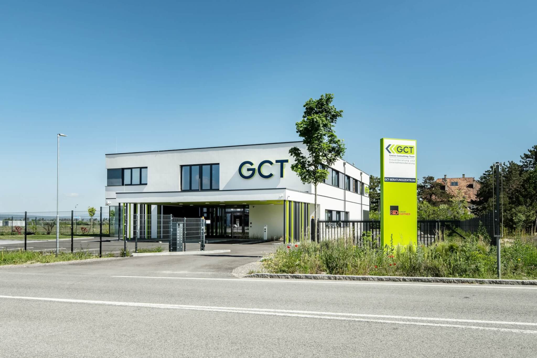 Modernes GCT-Bürogebäude für Steuer- und Unternehmensberatung mit grünem Schild, umgeben von Landschaft unter blauem Himmel.