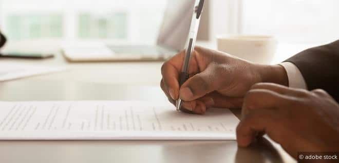 Hand unterschreibt einen Vertrag – Symbol für Steuern bei Kleinunternehmen in Österreich und rechtliche Verpflichtungen.