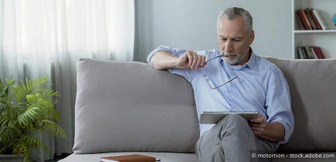 Älterer Herr sitzt nachdenklich auf dem Sofa und liest Unterlagen – Symbolbild für Teilpension.