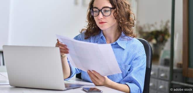 Frau liest vor dem Laptop Unterlagen durch – Symbolbild für Änderungen bei FinanzOnline.