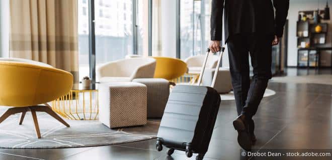 Mann schiebt seinen Trolley durch ein Hotelzimmer – Symbolbild für Ortstaxe.