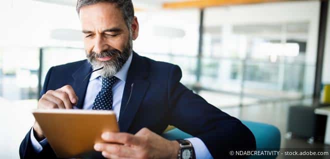 Mann im Anzug, der in ein Tablet tippt – Darstellung zum Thema Hälftesteuersatz für die Pensionsabfindung.
